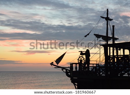 silhouette of a pirate ship with a captain behind steering wheel, looking through spyglass. (not an actual ship, imitation) Royalty-Free Stock Photo #181960667