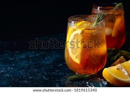 Traditional iced tea with lemon, lime and ice garnished with rosemary twigs. Frozen glasses with citrus slices on a dark blue table. Copy space.