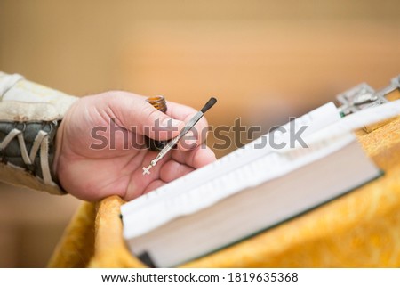 Priest's hand with anointing brush and bible.