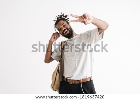 Photo of cheerful african american guy in headphones gesturing peace sign isolated over white wall