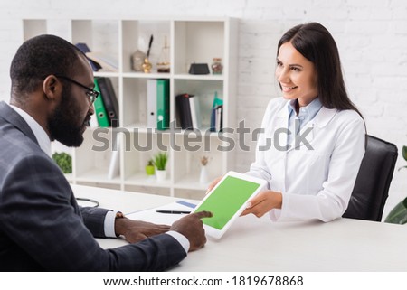 selective focus of african american man pointing with finger at digital tablet with green screen near brunette doctor