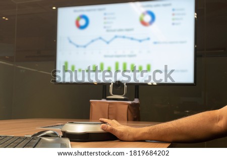 Man's hand is pressing the microphone button to speak with Presentation meeting on television in Video conference meeting room (Work from home Concept)