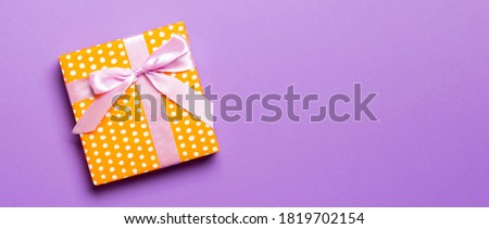 Top view Christmas present box with pink bow on purple background with copy space.
