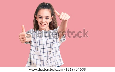 Cute hispanic child girl wearing casual clothes approving doing positive gesture with hand, thumbs up smiling and happy for success. winner gesture. 