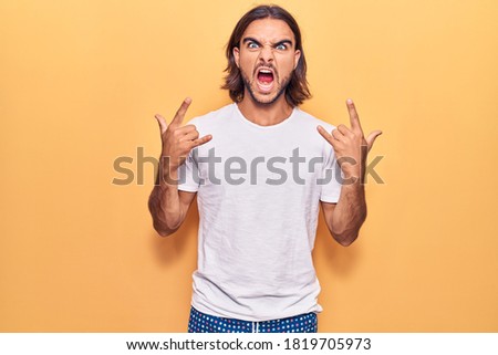 Young handsome man wearing casual clothes shouting with crazy expression doing rock symbol with hands up. music star. heavy concept. 