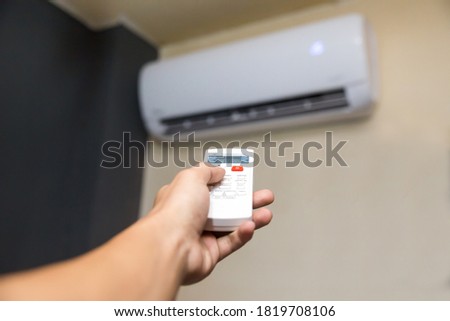 man's hand holding air conditioning unit remote control aimed at the AC unit  Royalty-Free Stock Photo #1819708106