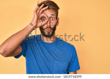 Handsome caucasian man with beard wearing casual clothes doing ok gesture shocked with surprised face, eye looking through fingers. unbelieving expression. 