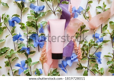 Mockup of pink squeeze bottle plastic tube with black cap, fresh greens, blue and pink flowers, silk ribbons on white background. Bottle for branding and label. Natural organic spa cosmetics concept.