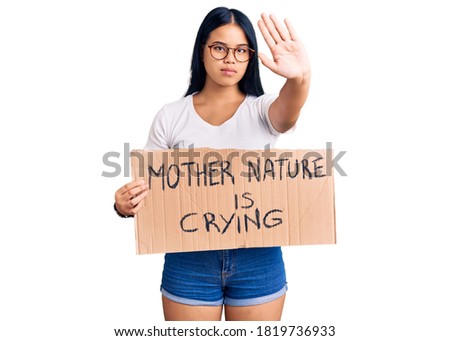 Young beautiful asian girl holding mother nature is crying protest cardboard banner with open hand doing stop sign with serious and confident expression, defense gesture 