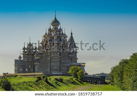 Historical, architectural and ethnographic open-air museum-reserve Kizhi. View of a wooden church, a bell tower and buildings on an island in Lake Onega. Green meadow around the complex.