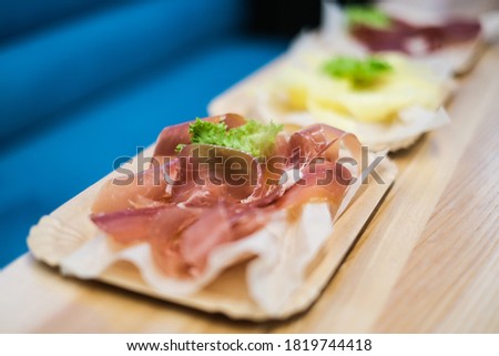 Cheese slices. Meat smoked jerky - raw meat sausage meat. Close up view on tasty sliced Chicken basturma on paper plate on a wooden background . Beer snack. Pastirma