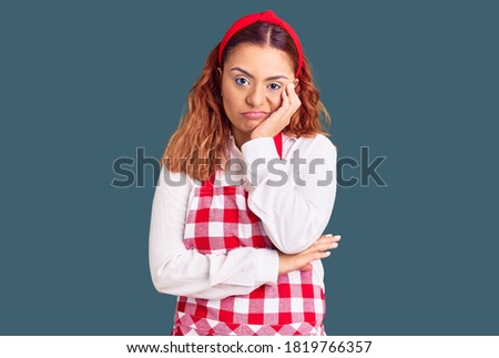Young latin woman wearing apron thinking looking tired and bored with depression problems with crossed arms. 