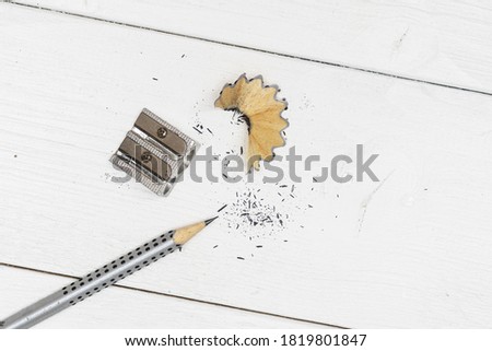 a pencil, a pencil sharpener and some shavings on a white wooden table