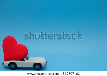 White retro toy car delivering a heart on a blue background. Postcard February 14, Valentine's Day. Flower delivery. March 8, International Happy Women's Day.