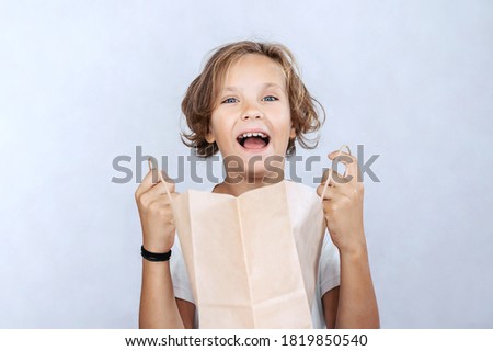 Emotional boy with paper bag on light background.
