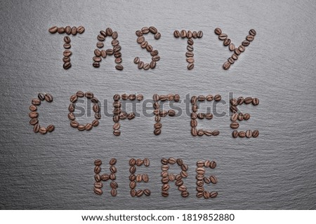 The inscription "Tasty coffee here" is lined with coffee beans. Rough grey stone background. 