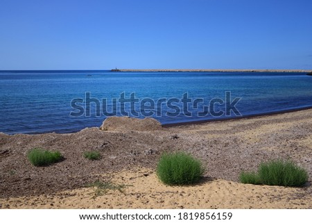 Scenic shot of the Mediterranean Sea, from a coast with little vegetation, of a harbor wall and small ships
