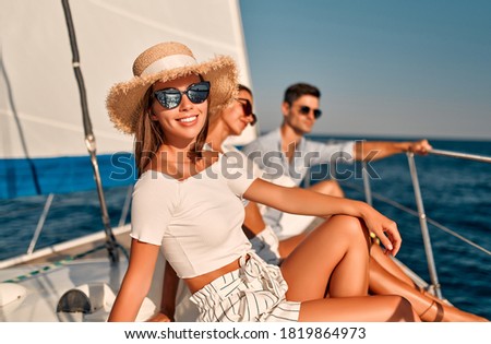 Group of friends relaxing on luxury yacht. Having fun together while sailing in the sea. Traveling and yachting concept. Attractive young woman in hat smiling and looking at camera on foreground Royalty-Free Stock Photo #1819864973