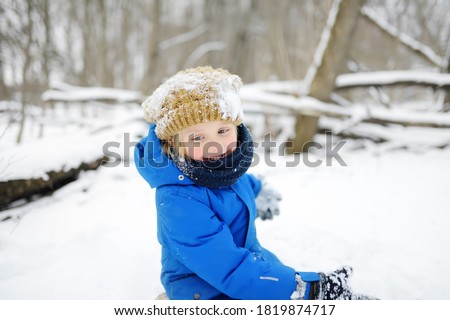Little boy having fun playing with fresh snow. Kid dressed in a warm clothes, hat, hand gloves and scarf. Active outdoors leisure for child on nature in snowy winter day.