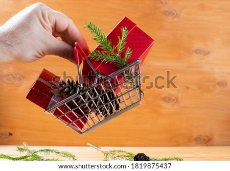 men hand keep miniature shopping cart on wheels loaded with boxes of gifts. wooden background with branches of a Christmas tree and cones. concept gifts for christmas and new year. copy space.