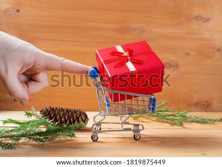 miniature shopping cart on wheels loaded with boxes of gifts. wooden background with branches of a Christmas tree and cones. concept gifts for christmas and new year. copy space.