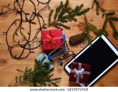 red gift box with bow, tablet, christmas tree branches, lights, wooden background. concept of gifts for christmas and new year. flat lay. copy space.