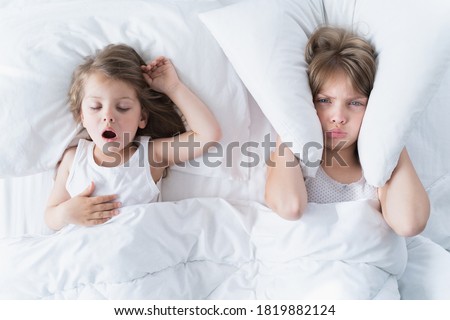 Little girls sleep in bed. One is snoring hard, sister is plugging her ears with pillow.  Royalty-Free Stock Photo #1819882124
