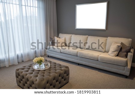 Blank white empty mock up template of a picture/art work with metal frame on living room/lounge wall with a neutral color sofa at front. Horizontal poster with copy space. Modern home/house interiors.
