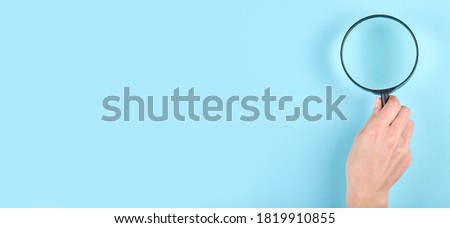 Hand with black magnifying glass on blue background. Flat lay, overhead view image. Copy space, template.