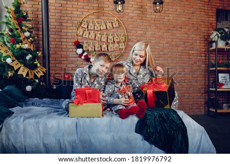 Beautiful mother in a gray pajamas. Family sitting on a bed. Little girl and boy near christmas tree
