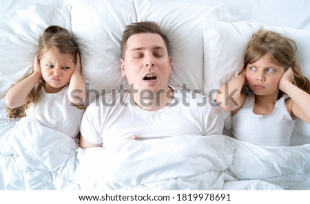 Kids, dad sleep together in bed. Father is snoring hard, girls, daughters are plugging ears with hands. Disorders, joint sleeping. Insomnia, night bedtime. Wake up, rise to kindergarten, school, work. Royalty-Free Stock Photo #1819978691