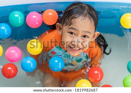Asian little girl playing with in the pool at house and coloured balls