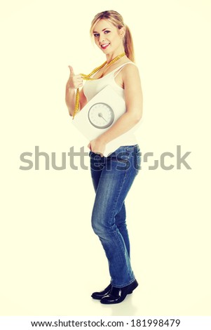 Woman with bathroom scale and measuring tape gesturing OK