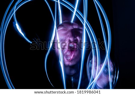 Long exposure on black background of adult white caucasian man with face illuminated with light painting technique. Concept of resentment, anger, madness, remorse, loneliness, mental disease.
