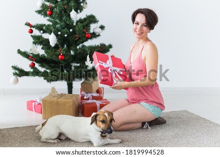 Happy woman with dog opening Christmas gifts. Christmas tree with presents under it. Decorated living room