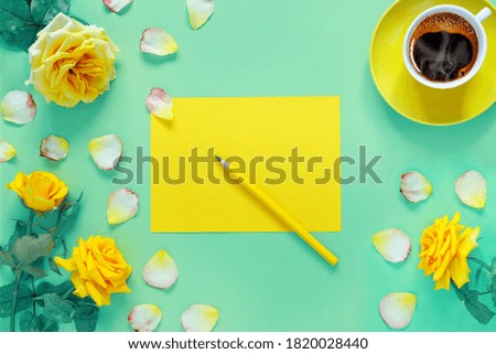 Bouquet of beautiful yellow roses and cup of hot fresh aromatic coffee on  green paper background. Notebook sheet  and  pencil for your text.
Flat lay, top view, copy space concept.