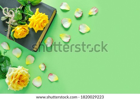 Beautiful bouquet of yellow roses with vintage book and flower petals on green table. Home office and sheet of paper for holiday invitation or congratulations.
Flat lay, top view, copy space concept.