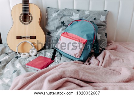 Student's room after study. Guitar, backpack, heaphones and notebook on the bed.