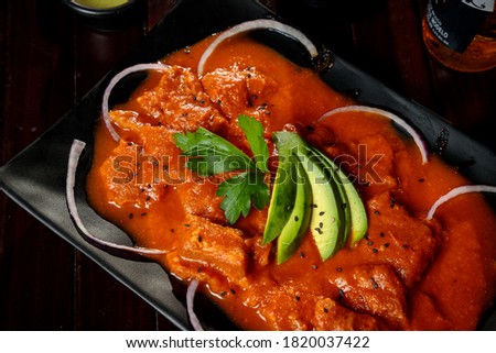 pork kind in red sauce with onion and avocado slices served on black plates