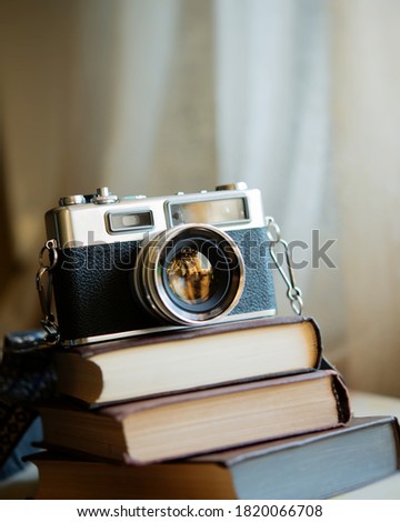 Three vintage books and a film camera are stacked on the table indoors. Books lie on a blurred background.