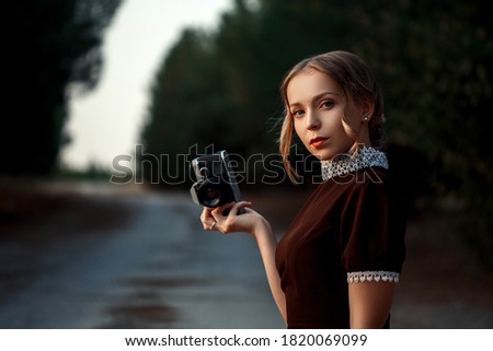 close-up portrait of a young beautiful girl in a brown dress in a retro style with a vintage camera in her hands on an abandoned road.