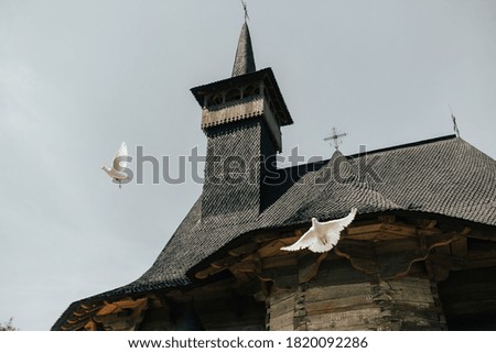 2 white doves fly in the background to the wooden church