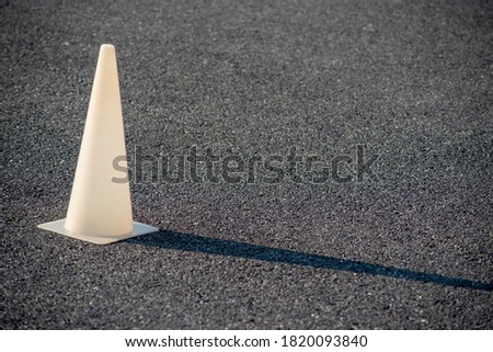Full frame image with copy space shot in natural light. White plastic cone glows in golden hour sun and casts a long shadow on the black asphalt.