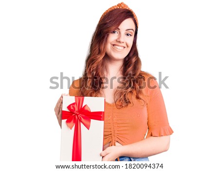 Young beautiful woman holding gift looking positive and happy standing and smiling with a confident smile showing teeth 