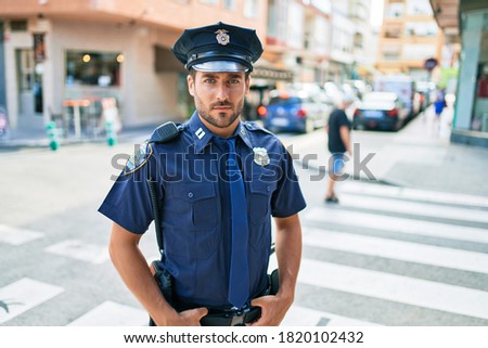 young handsome hispanic policeman wearing police uniform. Standing with serious expression at town street.