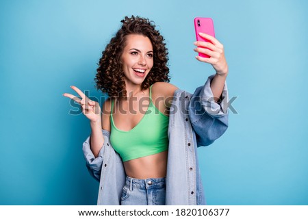Photo of positive cheerful youth woman blogger take selfie smartphone make v-sign enjoy youngster travel trip wear green jeans style stylish clothes isolated over blue color background