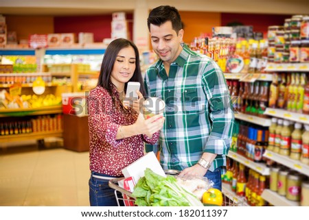 Pretty young brunette and her partner taking a picture of a product with her cell phone at a grocery store