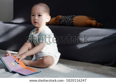 A little boy sitting on the carpet reading an early childhood picture book