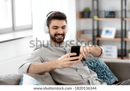 technology, leisure and people concept - happy man in headphones with smartphone listening to music at home