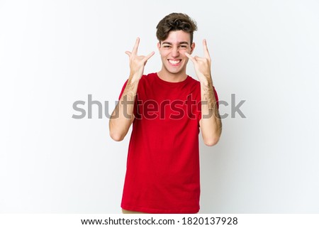 Young caucasian man isolated on white background showing a horns gesture as a revolution concept.